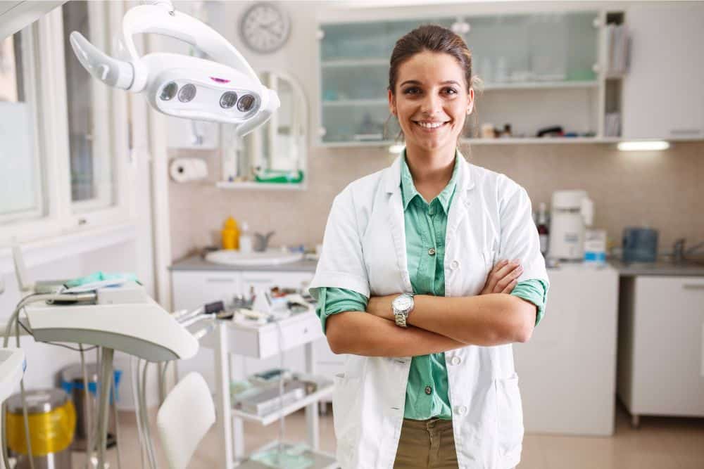 how to be THE dentist in your area Dentist standing in exam room looking at the camera and smiling