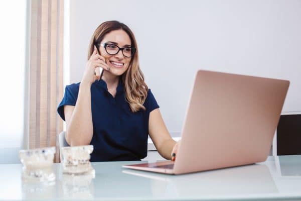 female dental professional talking on phone and working on laptop