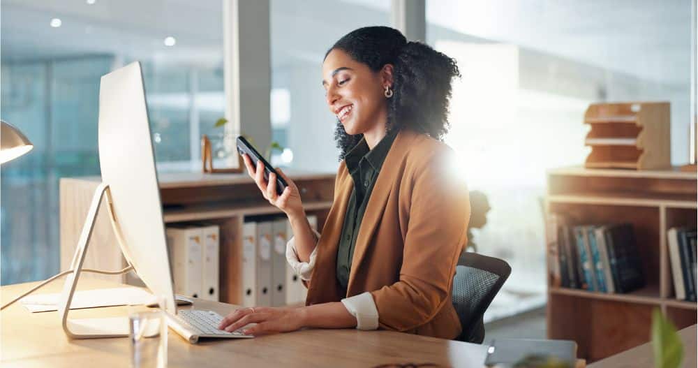 A receptionist sitting at her desk using her cell phone to contact a patient for a review