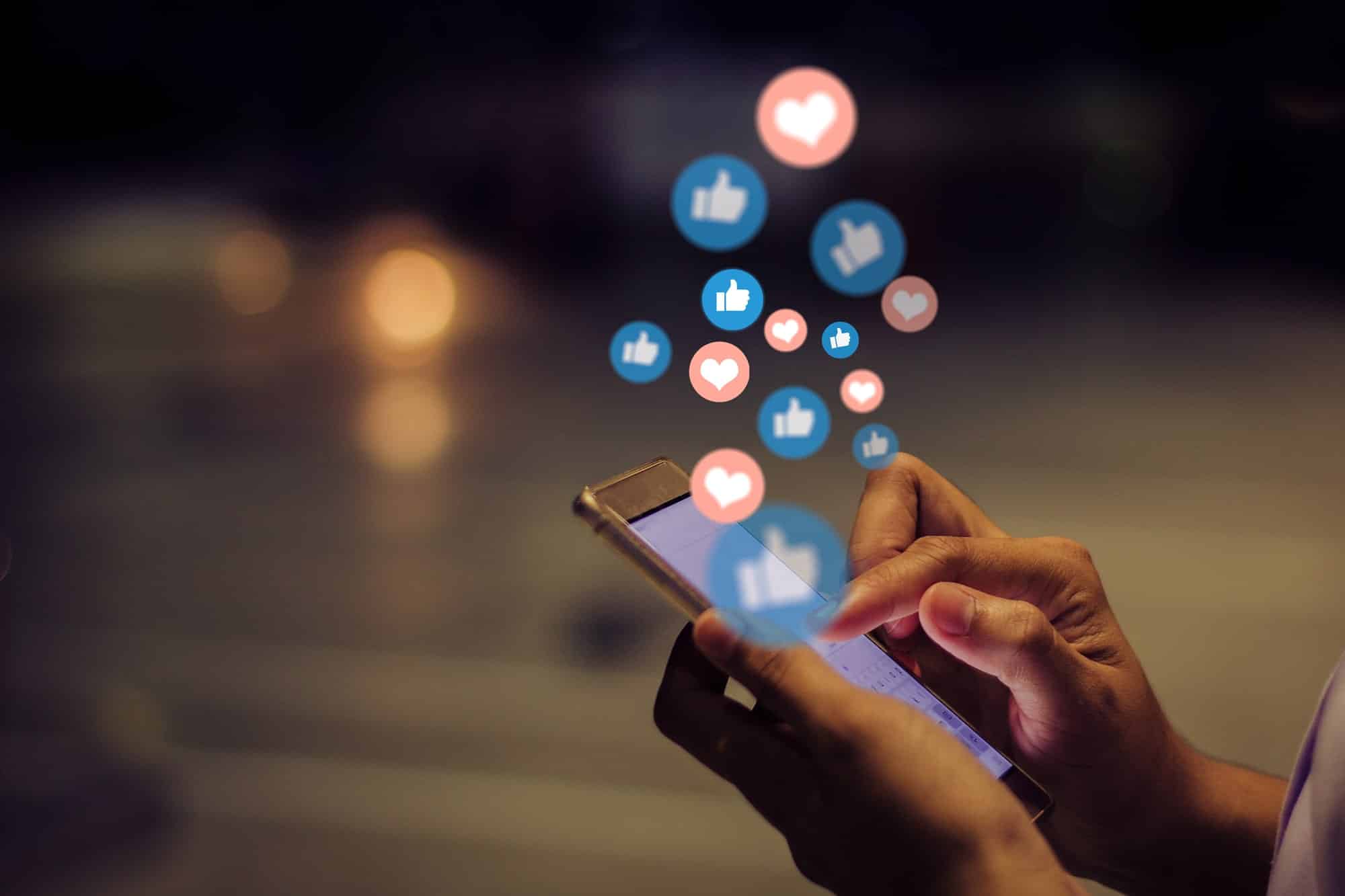 person on their phone with graphic thumbs-up and hear icons floating around