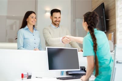 Happy dental patients greeting receptionist, reflecting strong reputation