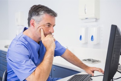 A dentist sitting at his computer looking deep in thought about something