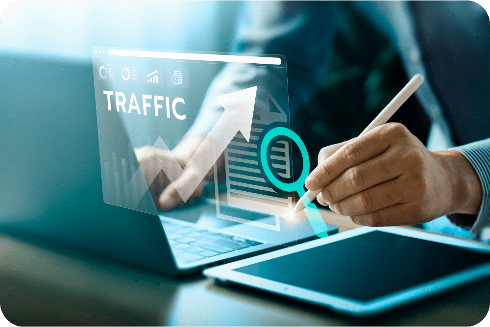 Person using a laptop and tablet with digital graphics showing “TRAFFIC” and an upward growth arrow.