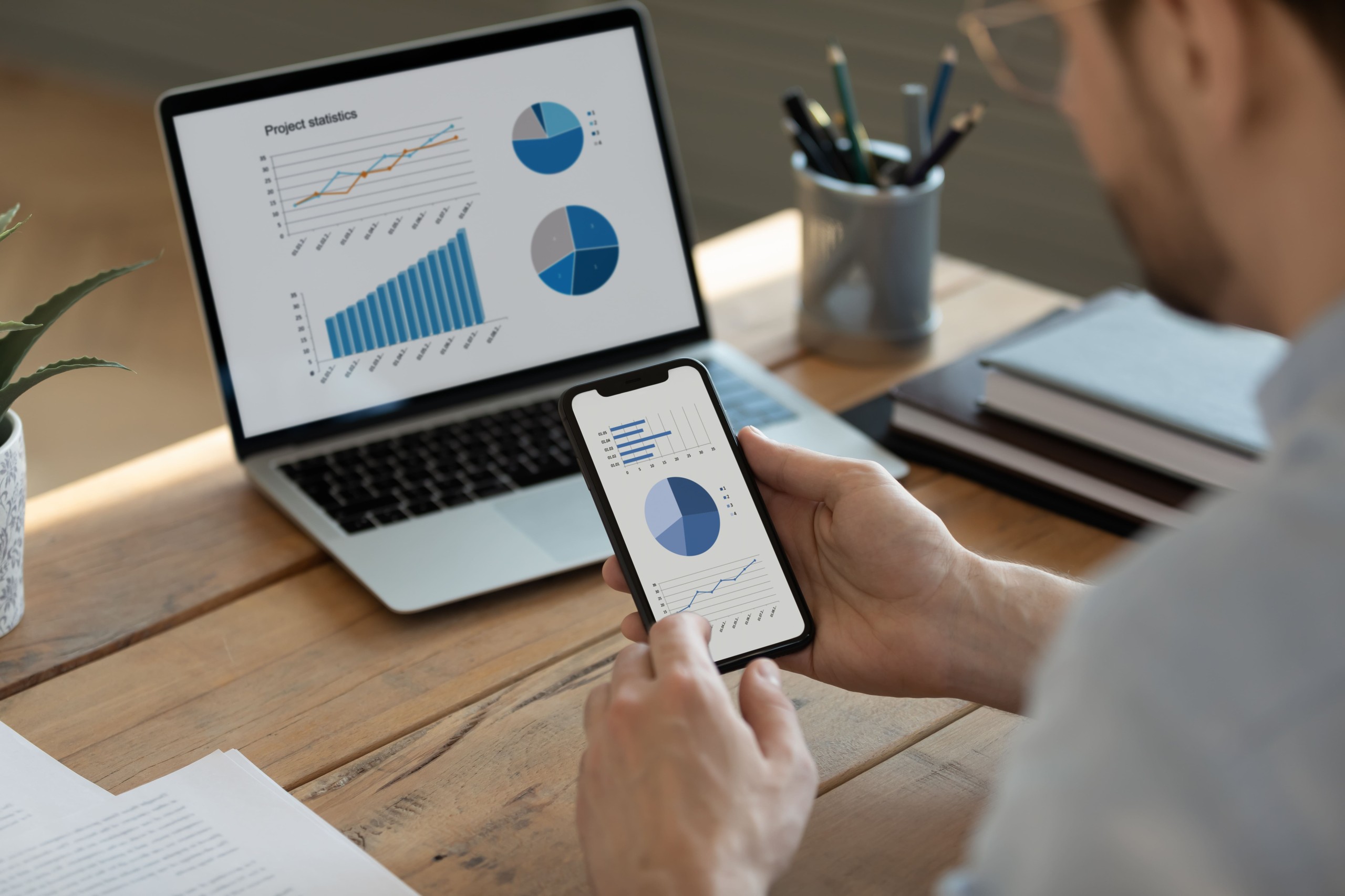 Person viewing project statistics with graphs and charts on a smartphone and laptop, representing data analysis or business reporting.