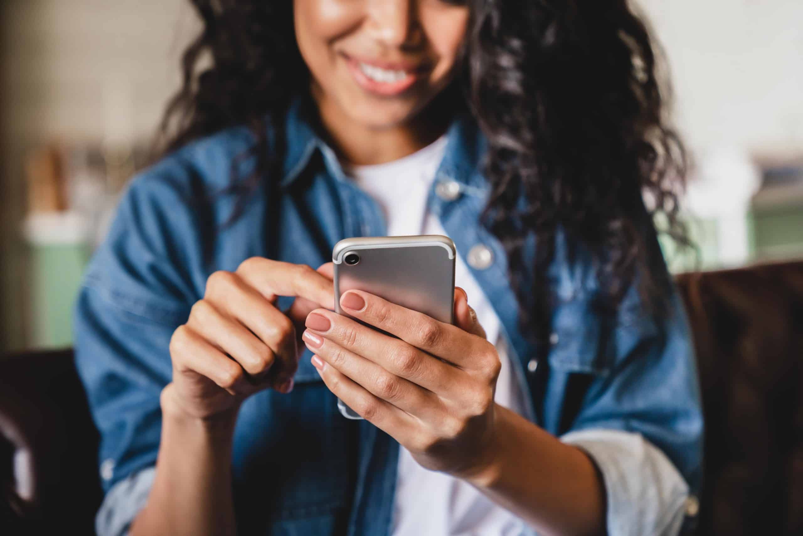 Smiling woman using a smartphone, suggesting casual browsing, texting, or social media use.
