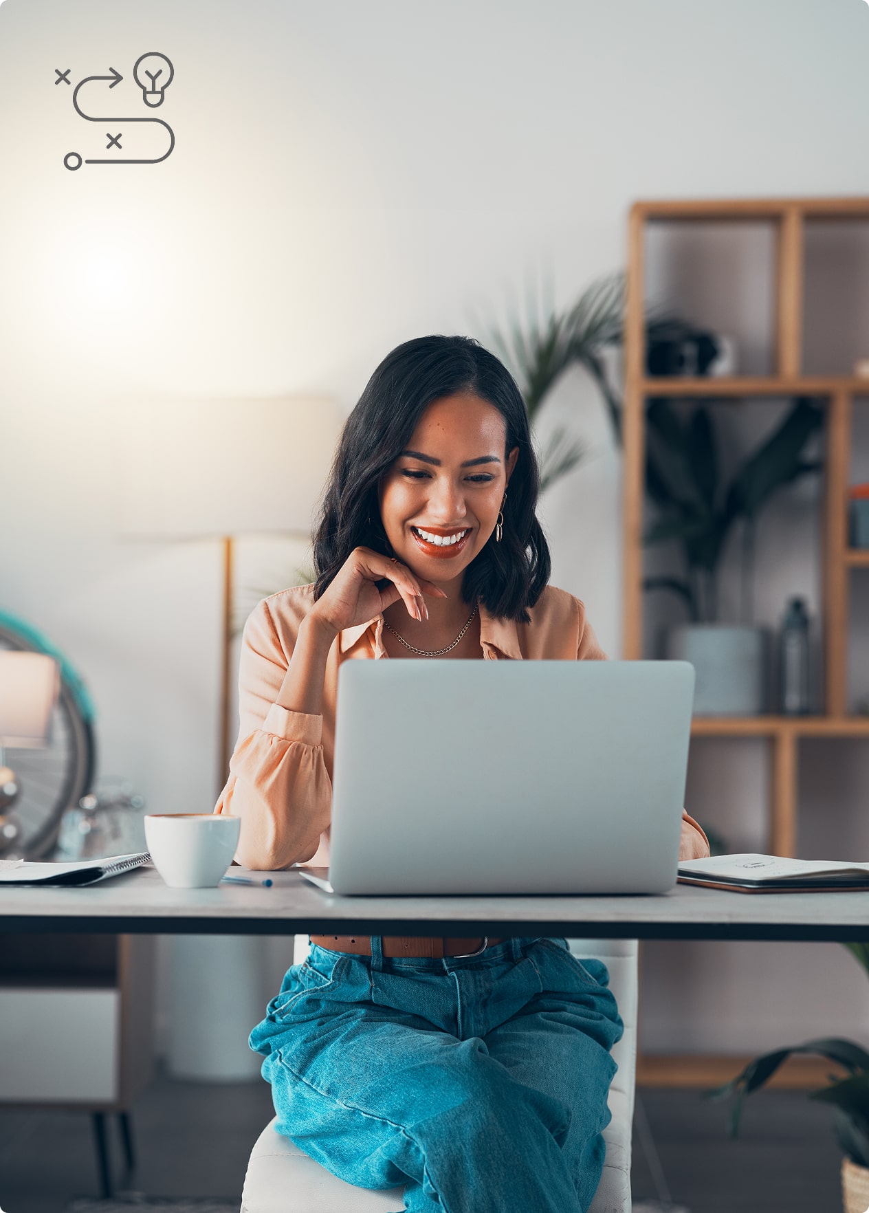 Group 288-min Smiling woman working on a laptop at home, with a cup of coffee and notebook, symbolizing productivity or remote work.
