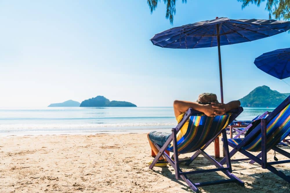 man relaxing on sandy beach in a chair with oversized umbrella